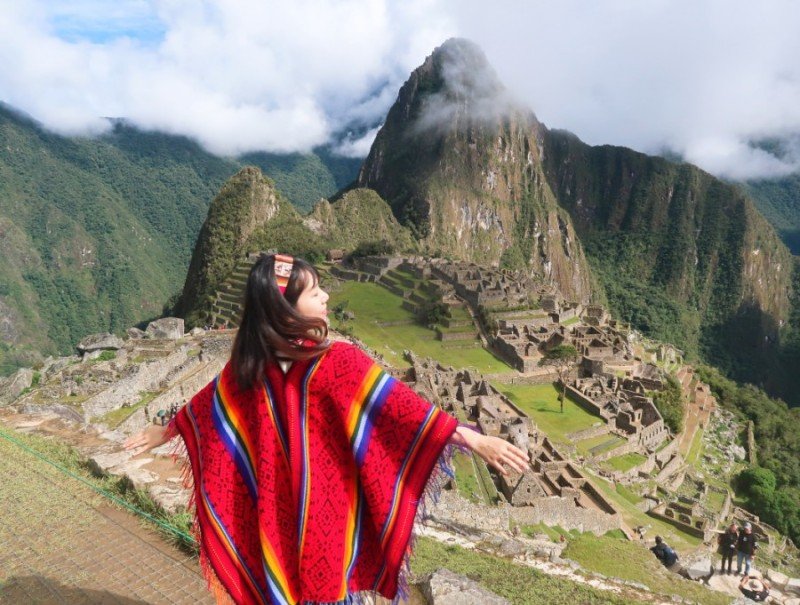 Ixchel in a red poncho above the Inca ruins of Machu Picchu, Peru.