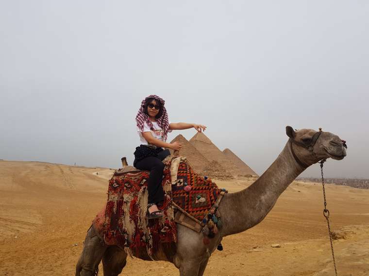 Ixchel riding a camel near the Pyramids of Giza, Egypt, 2018 — from her travel archive.